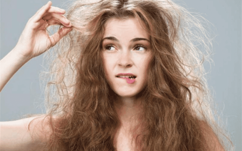 moça mordendo os lábios e passando a mão nos cabelos com frizz porque não sabe o que é leave-in