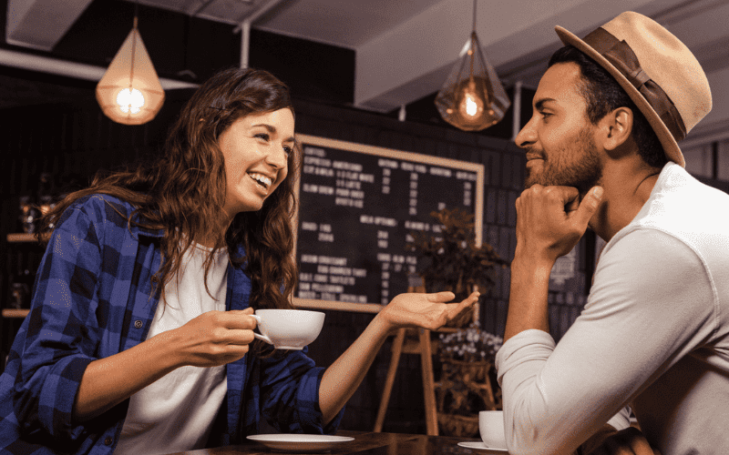 mulher conversando com homem. Ela gesticula sexy e sedutora, tomando café e ele olha para ela apaixonado