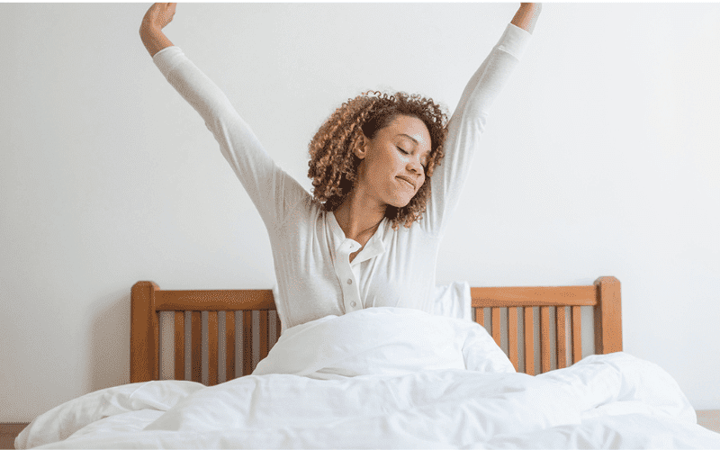 mulher acordando demanahã se espreguiçando em sua cama