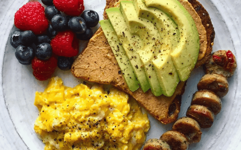 prato de cafe da manhã saudável com ovos, bananas picadas,1 fatia de pão com abacates, morangos e bluebery