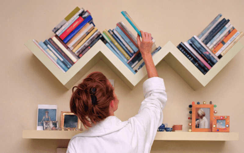 moça titrando um livro da sua estante com varios livros